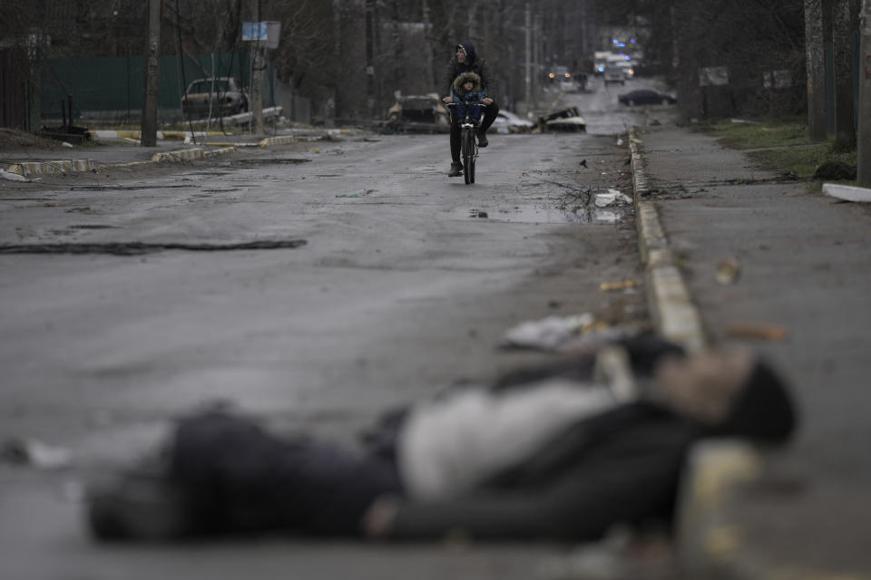 FILE - A man and child ride on a bicycle as bodies of civilians lie in the street in the formerly Russian-occupied Kyiv suburb of Bucha, Ukraine, Saturday, April 2, 2022. (AP Photo/Vadim Ghirda, File)