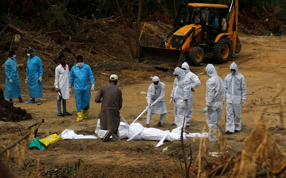 Relatives use ropes to lower the body of a person who died of COVID-19, into a freshly dug grave at a cemetery in New Delhi