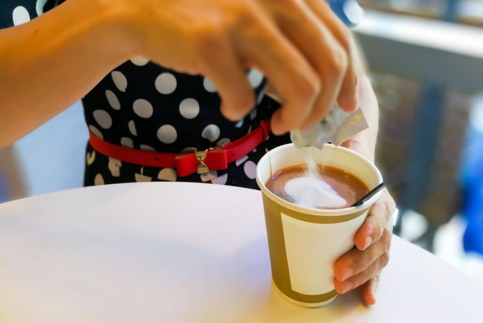 Woman pouring sugar into coffee