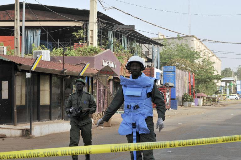 Policemen stand near the La Terrasse restaurant -- seen in the backround with the blue curtains -- in Bamako on March 7, 2015, after five people were shot dead overnight in a suspected terror attack
