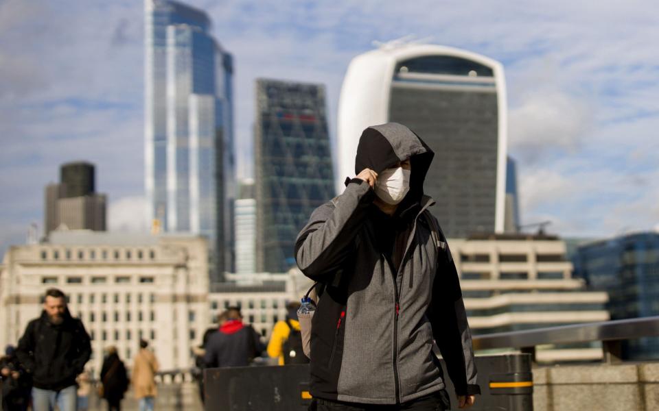 A man wearing a protective face mask, walks across London Bridge  - TOLGA AKMEN /AFP