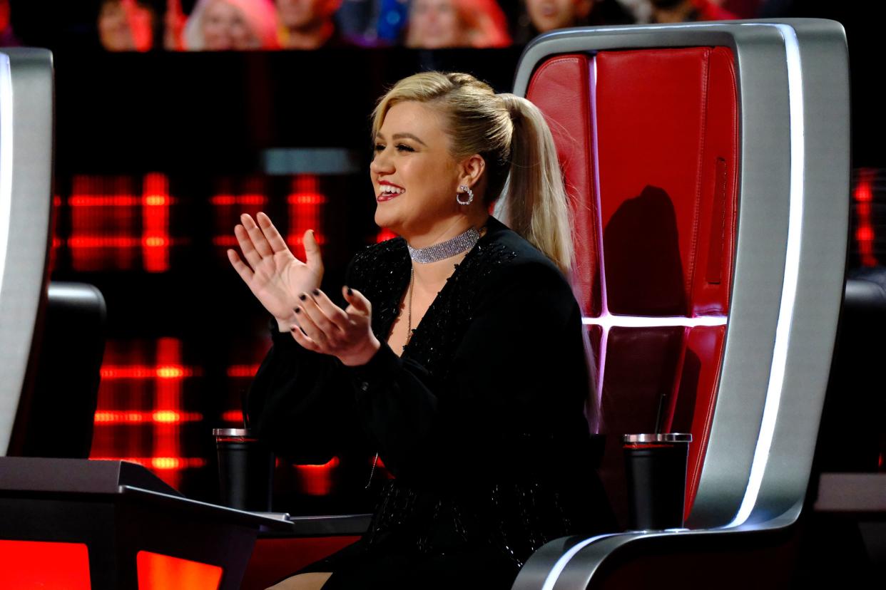 Kelly Clarkson sits on her The Voice chair mid-clap