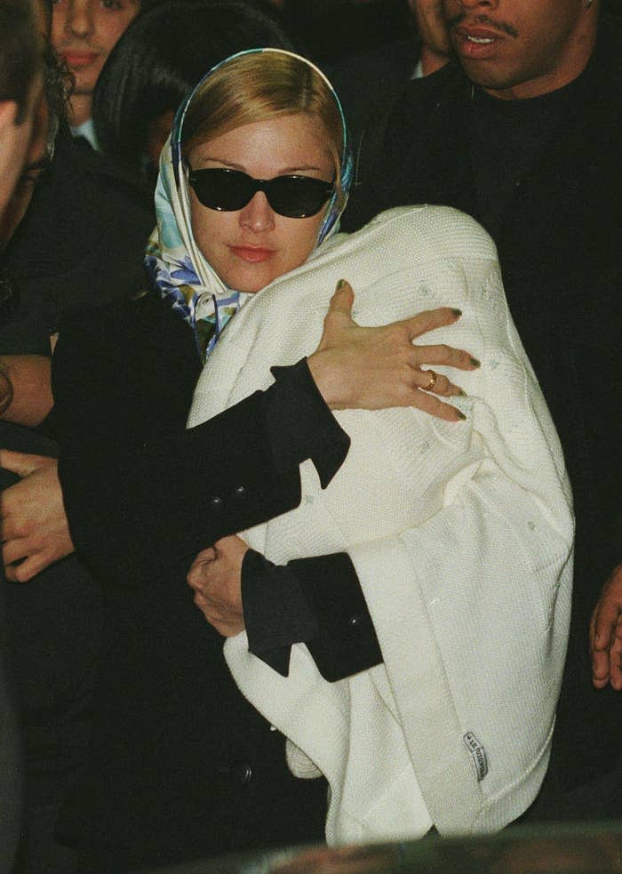 Madonna wearing a silk head wrap carrying a baby Lourdes in a blanket
