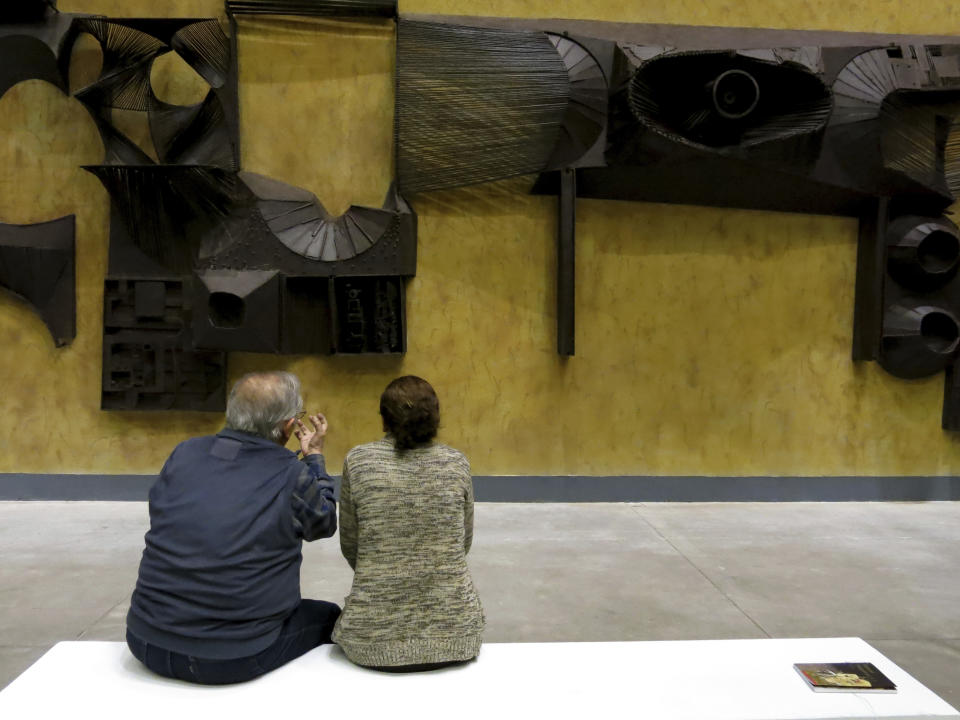 En esta fotografía del 7 de diciembre de 2019 visitantes observan la pieza “Mural de hierro” del artista mexicano Manuel Felguérez en la exposición "Trayectorias" del Museo Universitario de Arte Contemporáneo de la Universidad Nacional Autónoma de México (UNAM) en la Ciudad de México. La exposición celebra la trayectoria de Felguérez quien cumple 91 años este mes. (Foto AP/Berenice Bautista)