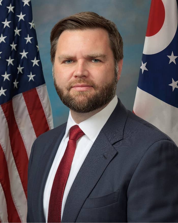 A man in a suit with a red tie stands in front of U.S. and Ohio flags