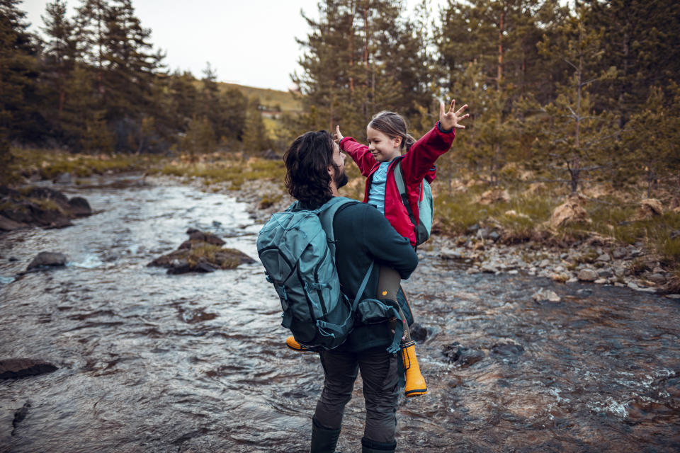 Close up of a father helping his daughter cross the stream while out hiking