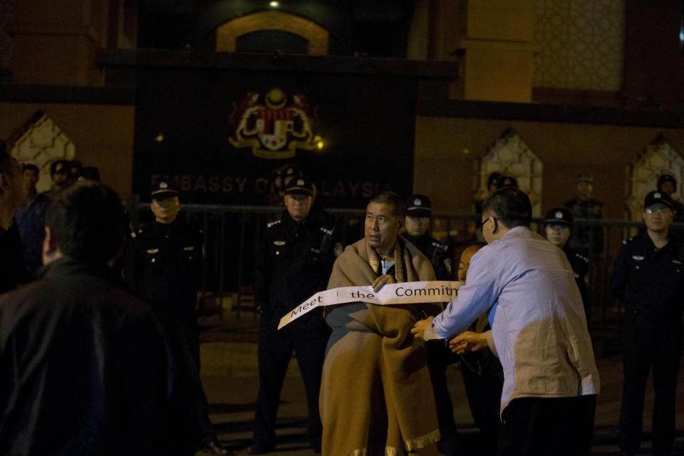 A relative of Chinese passengers onboard the Malaysia Airlines MH370 wrapped in a blanket against the cold holds up a sign which reads "Meet the Commitment" as he protest outside the Malaysia embassy in Beijing, China, Friday, April 25, 2014. Relatives angry at waiting for more than 8 hours in vain for a Malaysia embassy representative to attend their daily meeting marched to the Malaysia embassy and protested through the night. (AP Photo/Ng Han Guan)