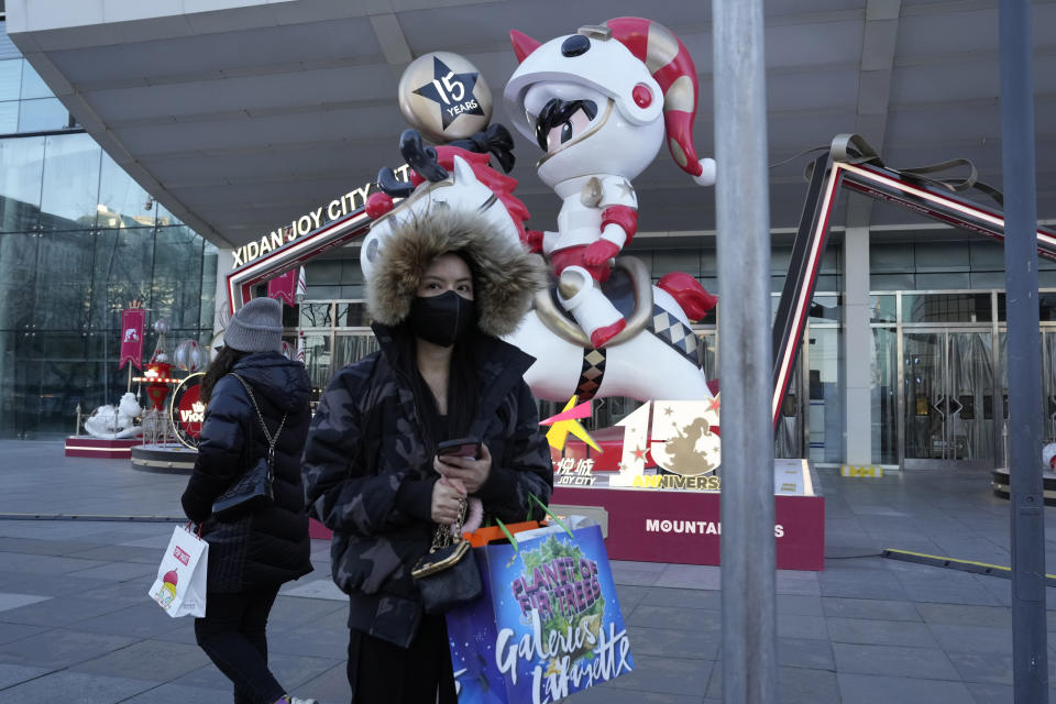 A shopper stands with her purchase near decorations outside a mall in Beijing, Thursday, Dec. 29, 2022. China is on a bumpy road back to normal life as schools, shopping malls and restaurants fill up again following the abrupt end of some of the world's most severe restrictions even as hospitals are swamped with feverish, wheezing COVID-19 patients. (AP Photo/Ng Han Guan)