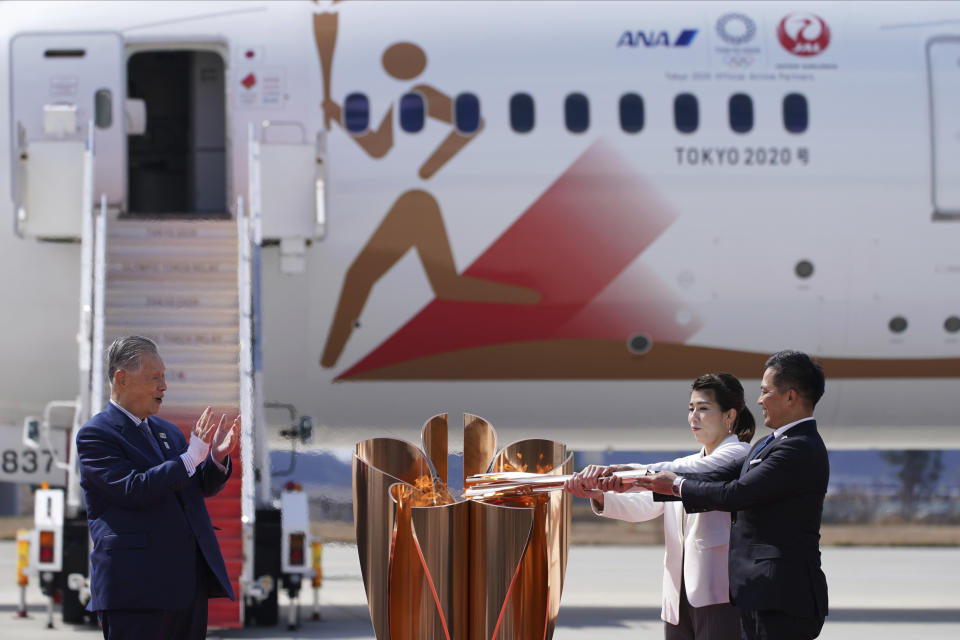 FILE - In this March 20, 2020, file photo, Olympic gold medalists Tadahiro Nomura, right, and Saori Yoshida light the torch as Tokyo 2020 Olympics chief Yoshiro Mori, left, watches during Olympic Flame Arrival Ceremony at Japan Air Self-Defense Force Matsushima Base in Higashimatsushima in Miyagi Prefecture, north of Tokyo. Tokyo Olympic organizers seem to be leaning away from starting the rescheduled games in the spring of 2021. More and more the signs point toward the summer of 2021. Organizing committee President Mori suggested there would be no major change from 2020. (AP Photo/Eugene Hoshiko, File)