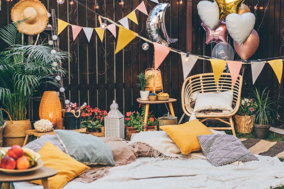 pillows and blankets set up outside in a backyard with chairs, lamps and decorations hanging around