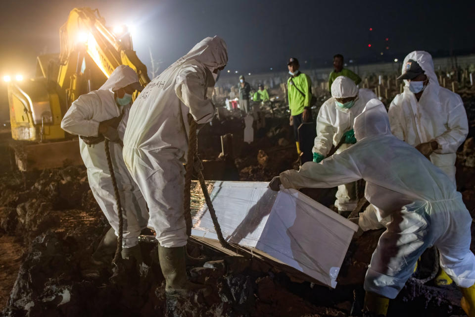 Undertakers wearing protective suits as a precaution lower the coffin of a Covid-19 victim for burial. Source: Sipa/AAP