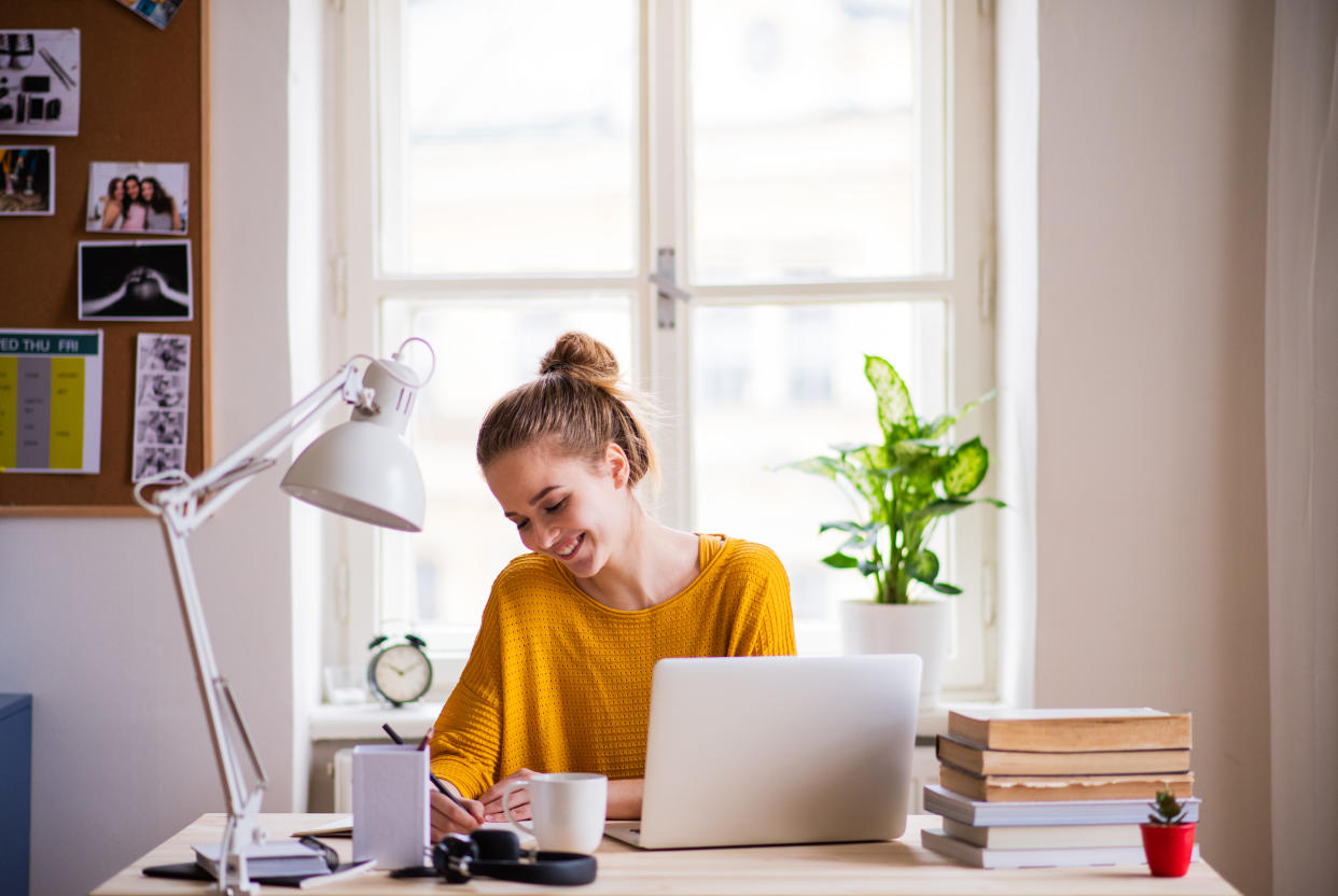 A young happy college female student sitting at the table at home, studying.