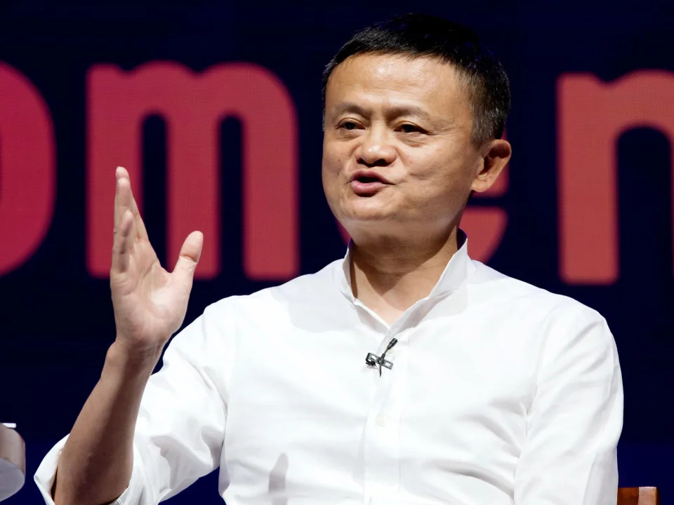 Jack Ma sitting on a stage and gesturing with his hand while speaking.