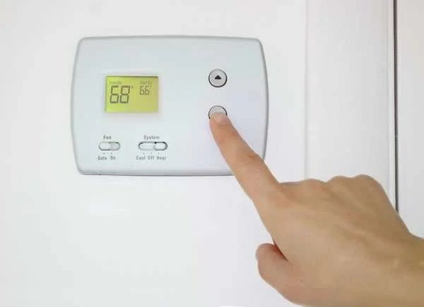 Person adjusting a digital thermostat to 68 degrees.