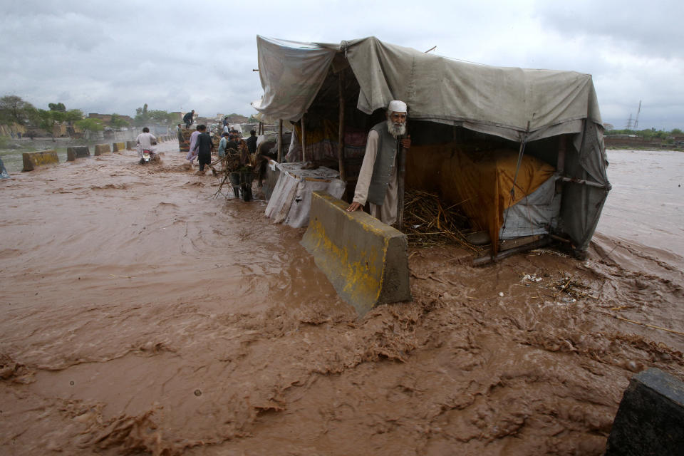 People stand beside a make shift stall set up on the bank of a stream, which is overflowing following heavy rains, on the outskirts of Peshawar, Pakistan, Monday, April 15, 2024. Lightnings and heavy rains killed dozens of people, mostly farmers, across Pakistan in the past three days, officials said Monday, as authorities declared a state of emergency in the country's southwest following an overnight rainfall to avoid any further casualties and damages. (AP Photo/Muhammad Sajjad)