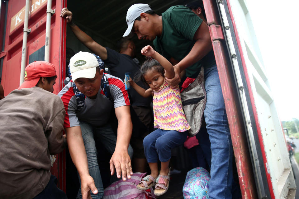 Migrants lift each other into the back of a truck.