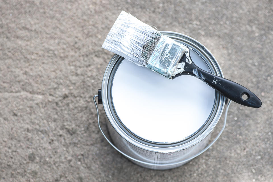 A can of white paint with a paintbrush on top of it.