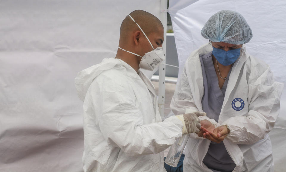 In this May 13, 2020 photo, Dr. Michel Martinez, right, sanitizes her hands before putting on medical gloves, as part of a sanitation protocol, before entering the respiratory evaluation unit in Tijuana, Mexico. Baja California Gov. Jaime Bonilla said in mid-April that the public health system’s doctors in the state were “dropping like flies” because they lacked protective gear. (AP Photo/Joebeth Terriquez)