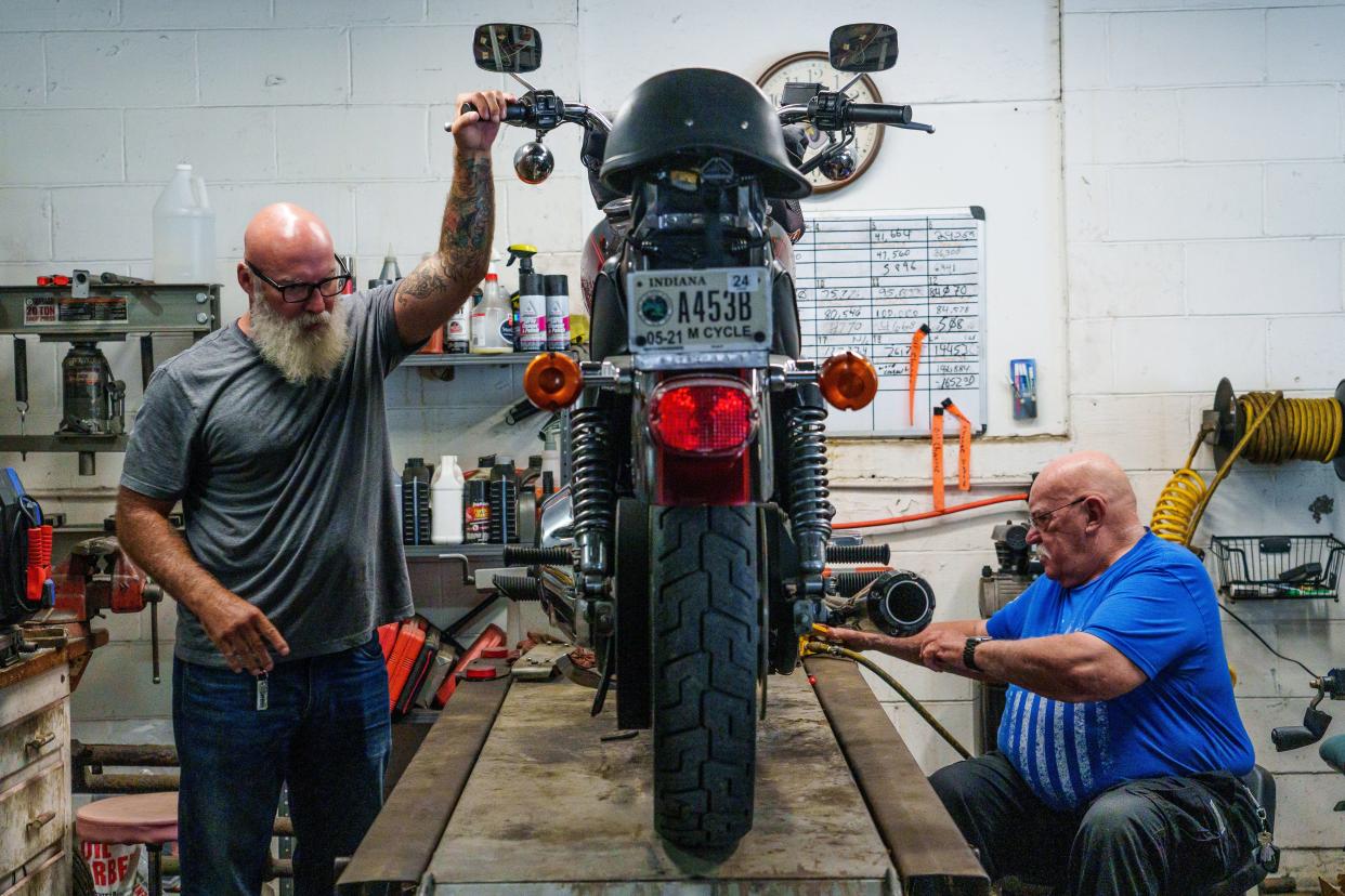 Gary Harriman (right), 71, a retired police officer, helps change the oil on his son Craig's Harley-Davidson motorcycle Thursday, June 29, 2023, at his shop in Indianapolis' Carson Heights neighborhood. Harriman owns and operates Indianapolis Funeral Escort Service alongside his wife, Michelle, who purchased the company in 2011. He and his team partner with 92 funeral homes across central Indiana to lead processions by motorcycle from funeral home to cemetery. Harriman says they will finish the month with 149 funeral processions.