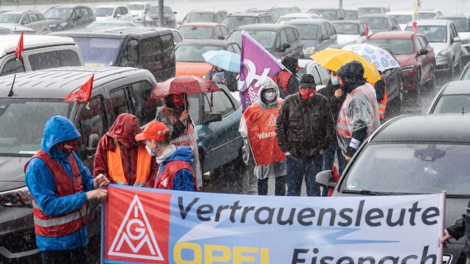 In strömendem Regen stehen Mitarbeiter am Stammsitz des Autobauers Opel oder sitzen in ihren Fahrzeugen, um gegen zunehmenden Druck an ihren Arbeitsplätzen zu demonstrieren.