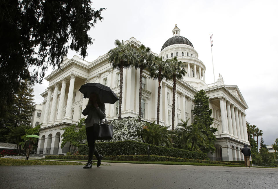 FILE - In this May 16, 2019, file photo a woman uses an umbrella as it rains at the Capitol in Sacramento, Calif. The California Legislature faces key decisions this week, including trying to reign in police use of force, prevent rent spikes, and alter labor laws affecting workers in the gig economy. (AP Photo/Rich Pedroncelli, File)