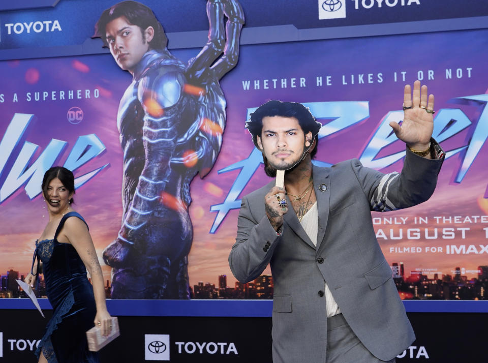 Angel Manuel Soto, right, director of "Blue Beetle," hides behind a cut-out of the film's star Xolo Mariduena as his wife Carla Gonzalez looks on at a screening of the film, Tuesday, Aug. 15, 2023, at the TCL Chinese Theatre in Los Angeles. Mariduena did not attend the premiere as per SAG-AFTRA guidelines during the current actors' strike. (AP Photo/Chris Pizzello)