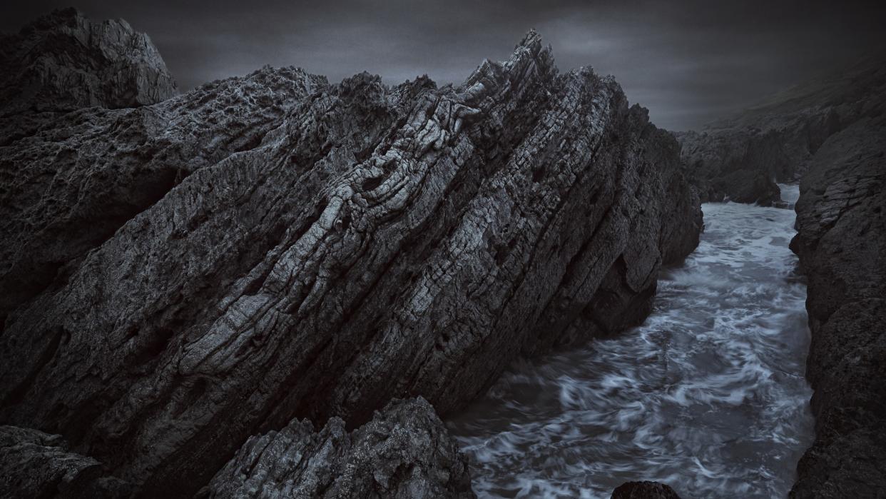  Water gushes through dark, craggy rocks on the shore. 