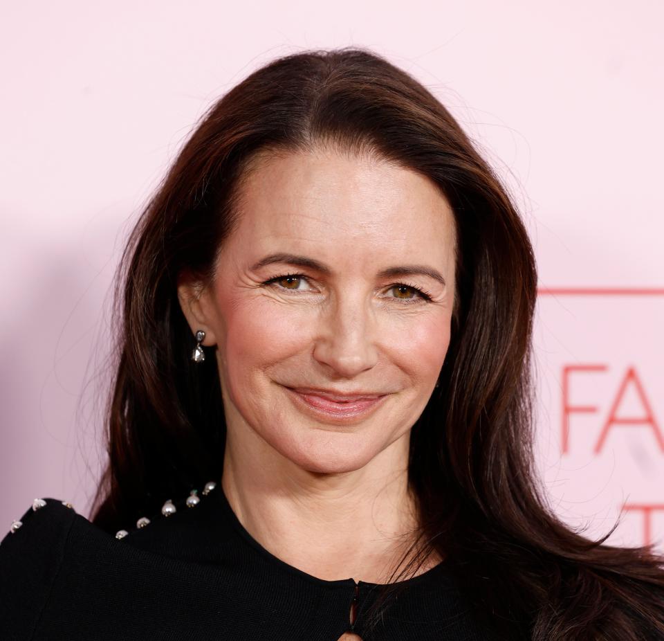 Kristin Davis in a dress with pearl details, smiling at a pink-background event