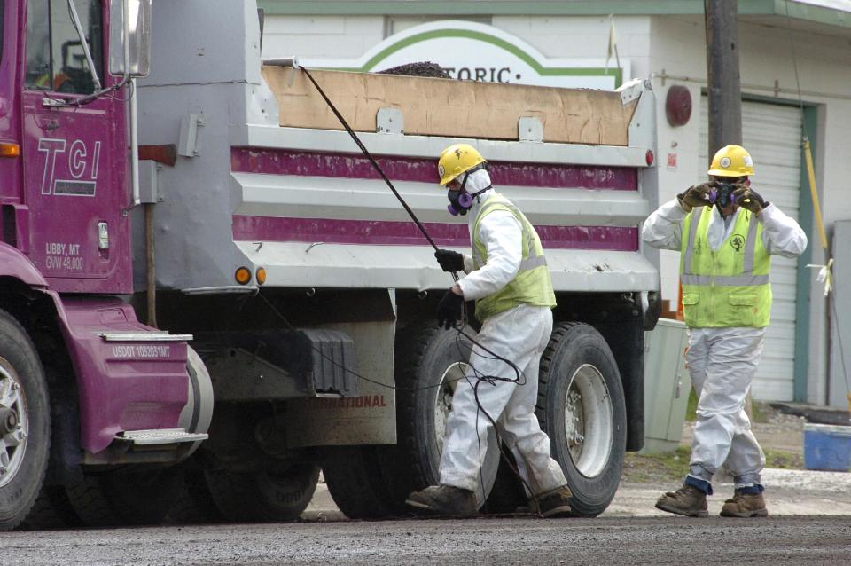 FILE - In this April 28, 2011 file photo, unidentified road workers wear protective gear against possible asbestos contamination as they load material from a road resurfacing project in downtown Libby, Mont. W.R. Grace, Inc., the chemical company blamed for polluting Libby, Mont. with asbestos dust that has killed hundreds of people, is pushing back against the Environmental Agency proposal and seeking to have it revised. Attorneys and scientists for W.R. Grace Inc., which operated an asbestos mine in Libby for three decades, say the EPA proposal would frustrate cleanup efforts by setting an unattainable standard for exposures. (AP Photo/Matthew Brown)