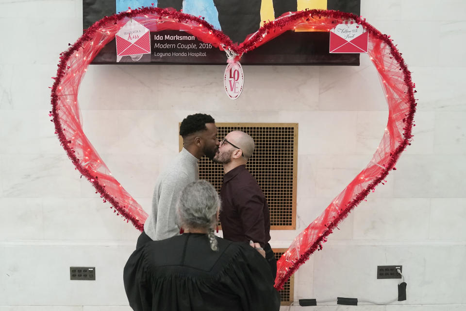 Jeremy Yancey, left, kisses Fabio de Andrade while getting married as deputy marriage commissioner Elba Clemente-Lambert, foreground, watches at City Hall in San Francisco, Tuesday, Feb. 14, 2023. In a state known to set the pace for the rest of the country on progressive policies, and one where its governor made news by issuing marriage licenses to same-sex couples while serving as the mayor of San Francisco, California lawmakers will attempt to enshrine marriage equality into the state's constitution. The effort comes 15 years after a voter-approved initiative, called Proposition 8, temporarily banned the state from recognizing same-sex marriages. (AP Photo/Jeff Chiu)