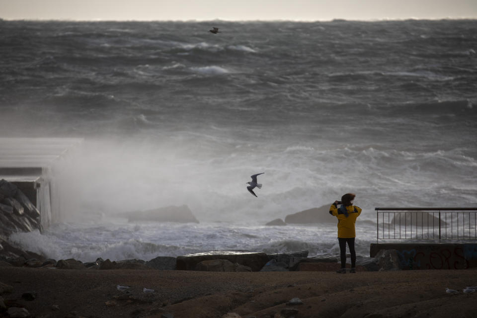 A woman photographs the Mediterranean sea during strong winds in Barcelona, Spain, Monday, Jan. 20, 2020. Two people have died as storms carrying heavy snowfalls and gale-force winds lashed many parts of Spain on Monday. The storm has forced the closure of Alicante airport and some 30 roads in eastern region. Six provinces are on top alert. (AP Photo/Emilio Morenatti)