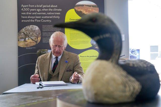 Charles with pen in hand as he prepares to sign a book, with a duck in the foreground