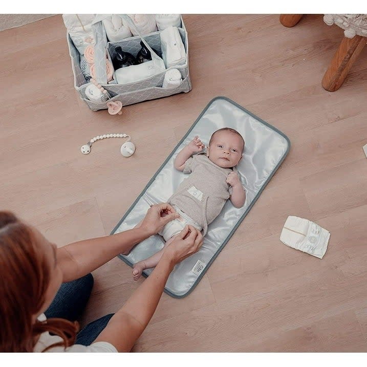 Model changing a baby's diaper on a portable changing mat with baby care products nearby