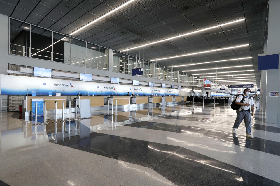 FILE - In this June 16, 2020, file photo, a traveler wearing a mask walks past empty American Airlines ticket counters in Terminal 3 at O'Hare International Airport in Chicago. American Airlines and four smaller carriers have reached agreement with the government for billions more in federal loans, a sign of the industry’s desperate fight to survive a downturn in air travel caused by the virus pandemic. The Treasury Department said Thursday, July 2, 2020, that it had finalized terms of new loans to American, Spirit Airlines, Frontier Airlines, Hawaiian Airlines and SkyWest Airlines. (AP Photo/Nam Y. Huh)