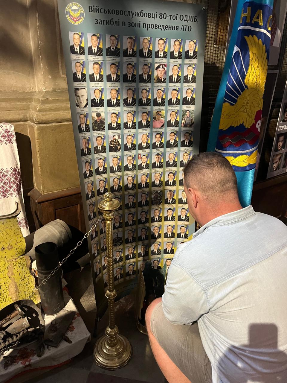 A Ukrainian soldier kneels in October 2023 before pictures of those killed near his hometown. The memorial is at St. Peter and Paul Garrison Church in Lviv, Ukraine.