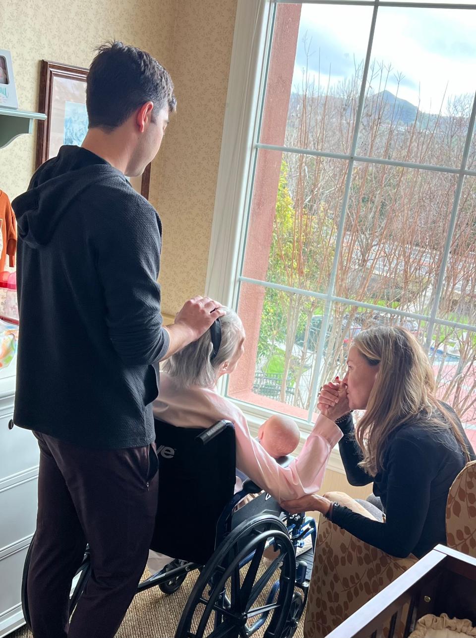 Barbara Rush with her daughter and grandson, looking out a window as she is seated in a wheelchair.