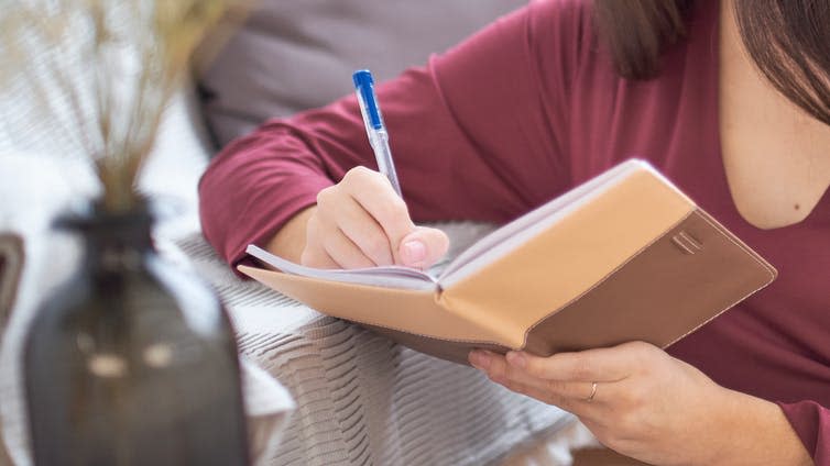 A woman writes in a notebook using a pen.