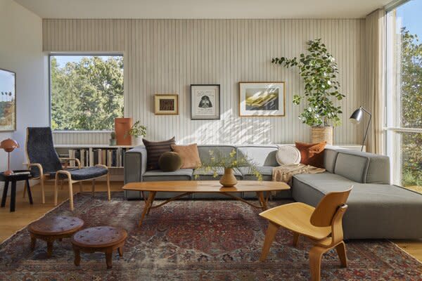 A BoConcept sectional is joined by a  Yngve Ekström lounge chair and ottoman and an Eames chair in the living area. The couple found the vintage Danish coffee table at a flea market, while the traditional Indian stools were purchased for their wedding. Whitewashed poplar clads the far wall.