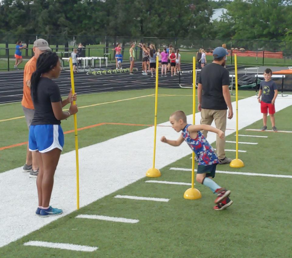 Brian Gentile weaves through a series of poles, including one held by Gardner High track and field alum Damali Waugh, during the Gardner Recreation Department's 2021 Youth Track and Field Clinic at Watkins Field in Gardner.