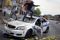 Demonstrators jump on a damaged Baltimore police department vehicle during clashes in Baltimore, Maryland April 27, 2015. REUTERS/Shannon Stapleton