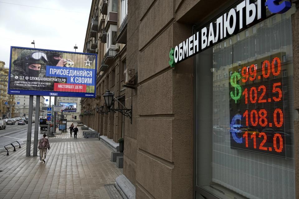 FILE - People walk past a currency exchange office with an army recruiting billboard calling for a contract for service in the Russian armed forces in Moscow, Russia,on Aug. 14, 2023. The central bank's rate hikes have cooled the ruble's exchange rate deterioration to a small extent, the rate is now about 88 to the US dollar, whereas earlier it had exceeded 100 to the dollar. But that's still far higher than in the summer of 2022, when it was about 60 to the dollar. (AP Photo, File)