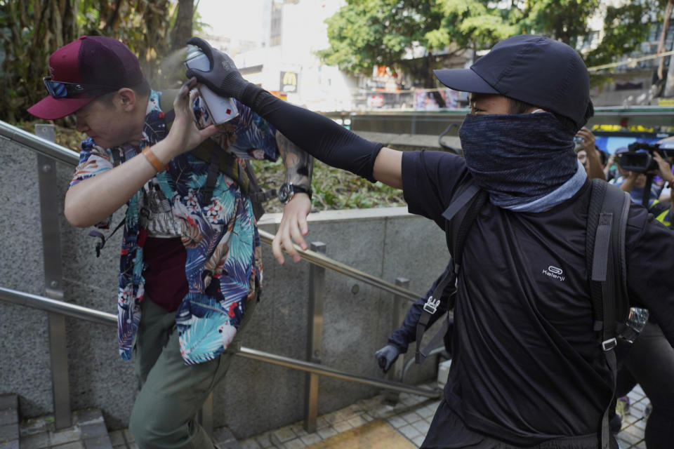 A protester sprays on a man who was trying to stop them for vandalizing near the Tsim She Tsui police station during a rally in Hong Kong, Sunday, Oct. 20, 2019. Hong Kong protesters again flooded streets on Sunday, ignoring a police ban on the rally and demanding the government meet their demands for accountability and political rights. (AP Photo/Vincent Yu)