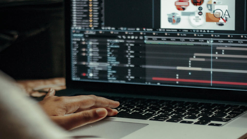 A hand on a laptop keyboard with the screening showing Adobe Creative..