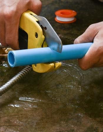 A close up of a person's hands using a yellow tool to cut a blue pipe.