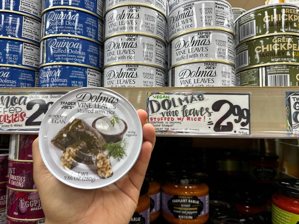 hand holding tin of greek dolmas in front of a shelf of tinned foods at trader joes