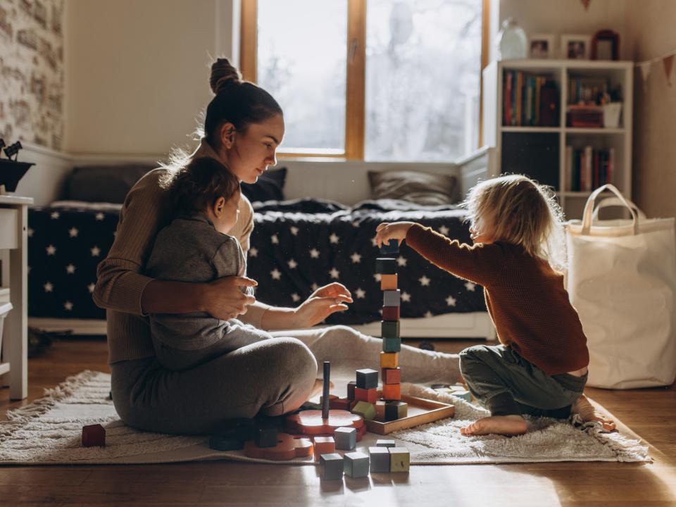 Young Mother playing with children while sitting on floor at home with wooden toys