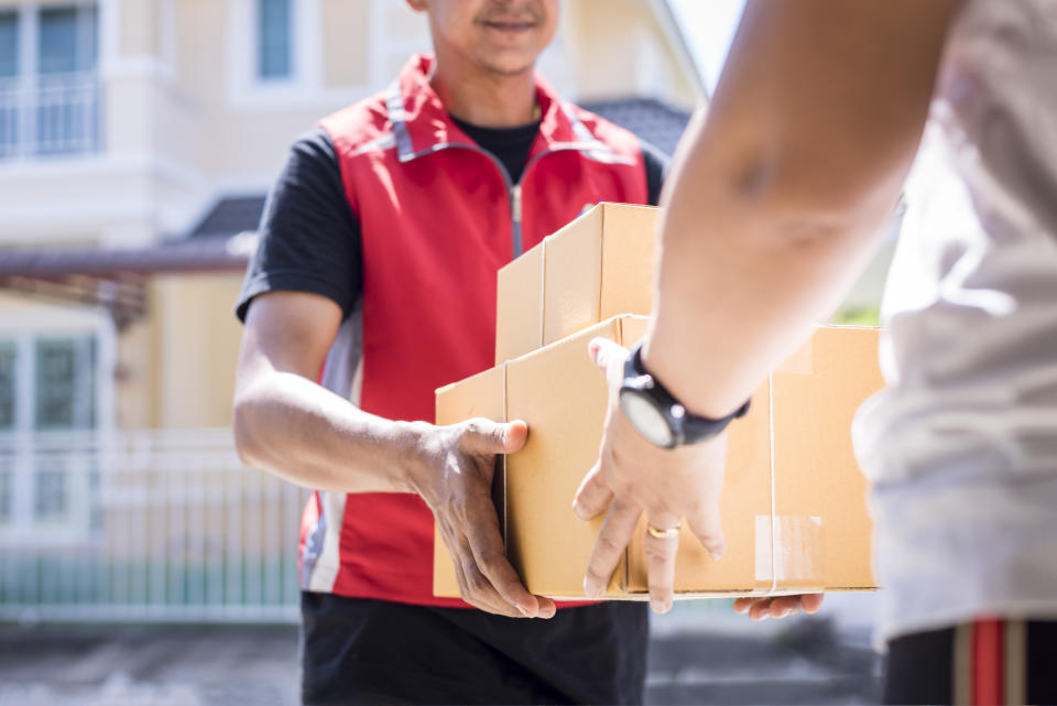 parcel delivery man of a package through a service and customer hand accepting a delivery of boxes from delivery man.