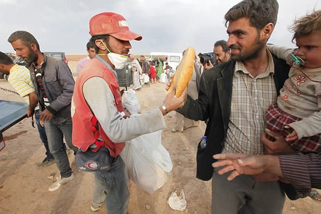 An aid worker gives a loaf of bread to the newly arrived Syrian Kurdish refugees as they walk with their belongings after crossing into Turkey. Photo: Getty