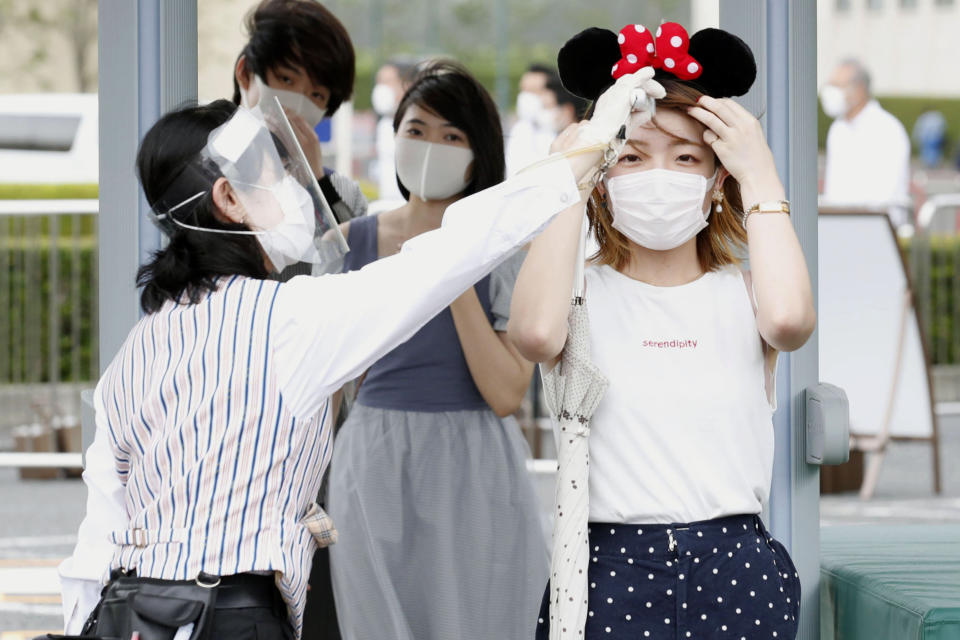 A visitor has her body temperature checked at the entrance of Tokyo Disneyland in Urayasu, near Tokyo, Wednesday, July 1, 2020. Tokyo Disneyland reopened for the first time in four months after suspending operations due to coronavirus concerns. (Kyodo News via AP)