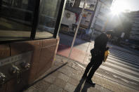 A man wearing a face mask looks at his cellphone while waiting to walk across an intersection during the coronavirus state of emergency in Tokyo on Thursday, Jan. 14, 2021. (AP Photo/Hiro Komae)